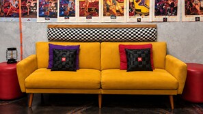 A yellow sofa with checkered cushions, a red stool, and a wall with calendars. - Downtown Chop Shop house, HUGE garage pets allowed (fort smith)