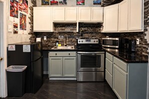 A compact kitchen with white cabinets, a black refrigerator, stainless steel appliances, and a backsplash with a geometric pattern. - Downtown Chop Shop house, HUGE garage pets allowed (fort smith)
