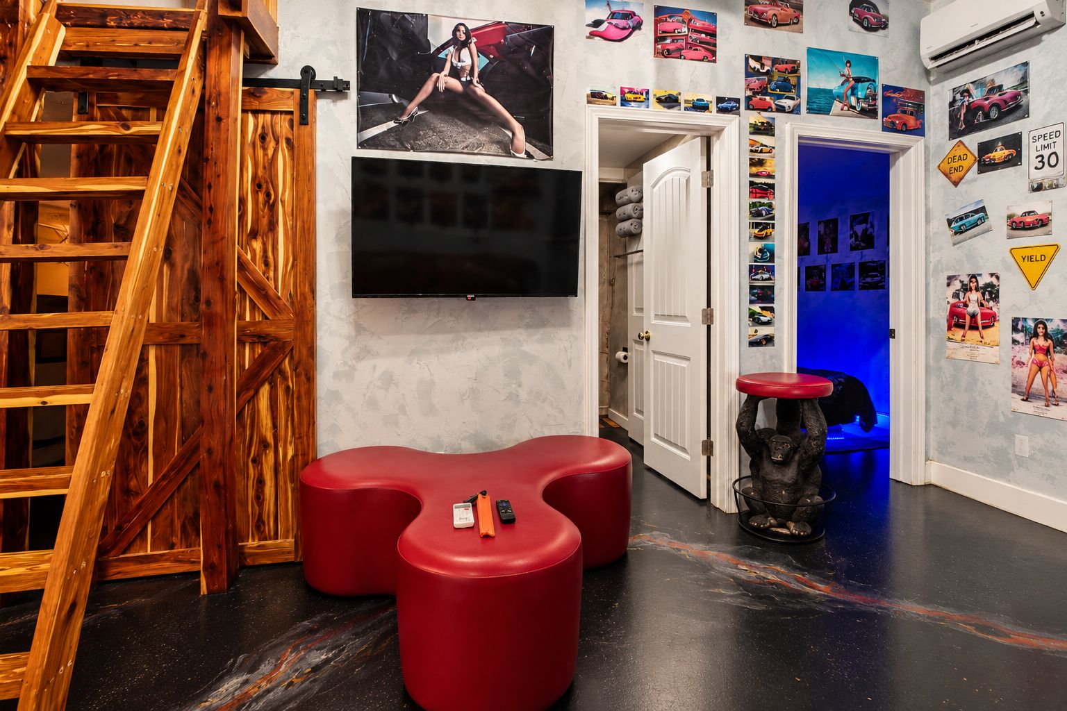 Une pièce avec un escalier en bois, un téléviseur à écran plat, des sièges rouges et un mur décoré de posters de voitures.