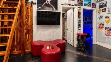 Une pièce avec un escalier en bois, un téléviseur à écran plat, des sièges rouges et un mur décoré de posters de voitures.