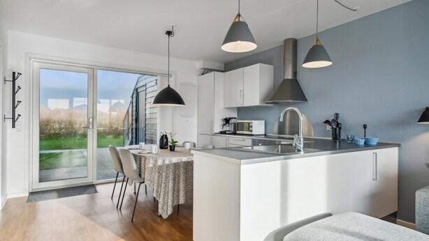 A modern kitchen with a large island, a dining area with a table and chairs, and a view of the outdoors through a sliding door. - Stunning apartment in Ringkøbing (Ringkøbing)