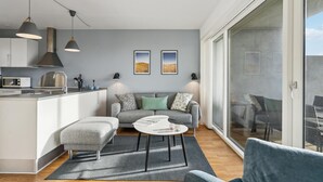 A modern living space with a kitchen, a grey sofa, a coffee table, and a view through a glass door. - Stunning apartment in Ringkøbing (Ringkøbing)