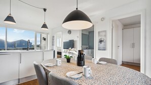 A modern kitchen with white cabinets, a dining table with a floral tablecloth, and a view of the mountains. - Stunning apartment in Ringkøbing (Ringkøbing)