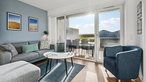 A modern living room with a grey sofa, a round coffee table, and a blue armchair. There are two framed pictures on the wall and a large sliding glass door leading to an outdoor area. - Stunning apartment in Ringkøbing (Ringkøbing)