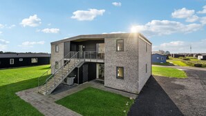 A modern building with a flat roof, a staircase leading to a balcony, and a small outdoor area with a paved path. - Stunning apartment in Ringkøbing (Ringkøbing)