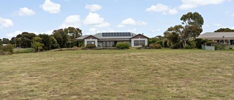 A modern two-story house with a large front lawn, solar panels on the roof, and a well-maintained garden.