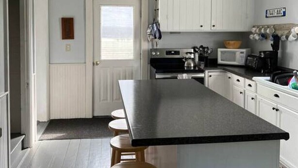 A kitchen with a central island, white cabinets, a ceiling fan, and a microwave. - The Webster House Vacation Station (Vinalhaven)