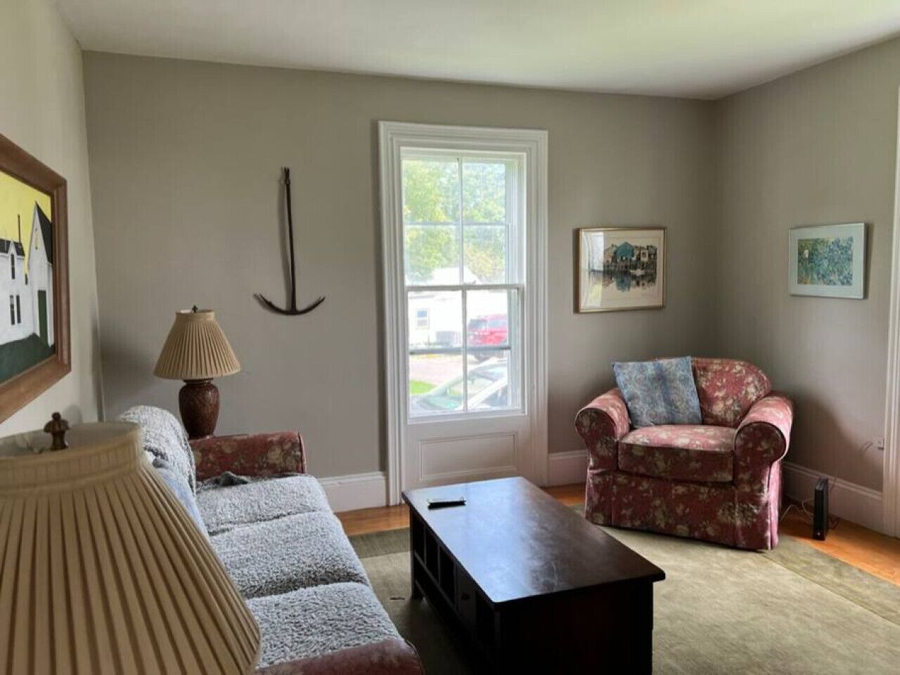 A living room with a sofa, armchair, coffee table, lamp, and paintings on the walls.