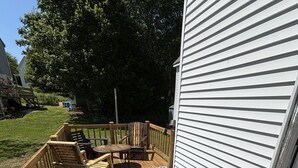 A wooden deck with a blue patterned rug, wooden chairs, and a table. - The Webster House Vacation Station (Vinalhaven)