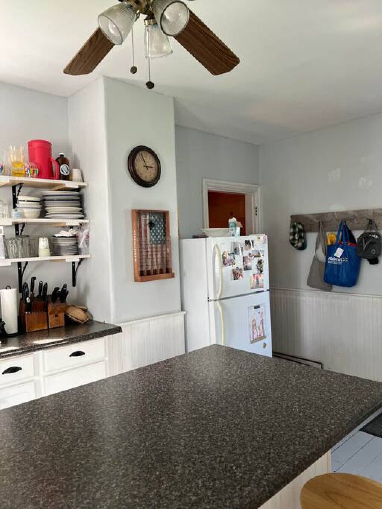 A kitchen with a granite countertop, white cabinets, a clock, and a ceiling fan.