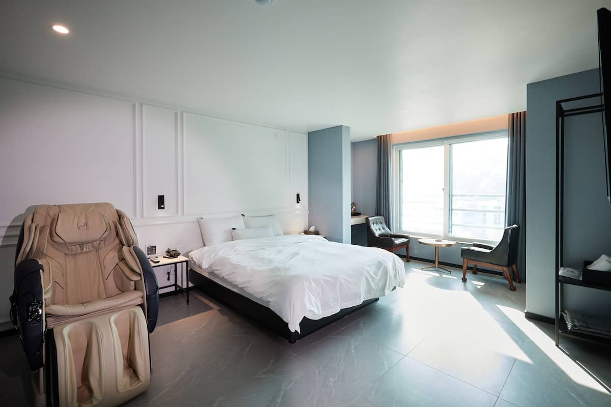 Ein modernes Hotelzimmer mit Bett, Massagesessel, Schreibtisch und großen Fenstern.