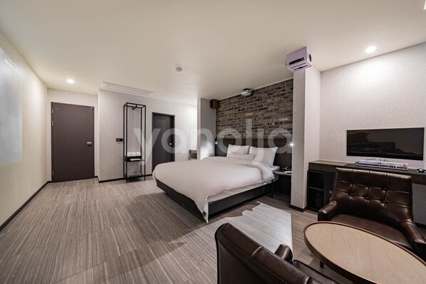 Ein modernes Hotelzimmer mit einem großen Bett, einer Sitzecke mit Stuhl und Tisch, einem Flachbildfernseher und einer Wand mit Ziegeloptik.