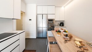 Een moderne keuken met witte kasten, een roestvrijstalen koelkast, een oven en een houten eettafel met vers fruit en brood.