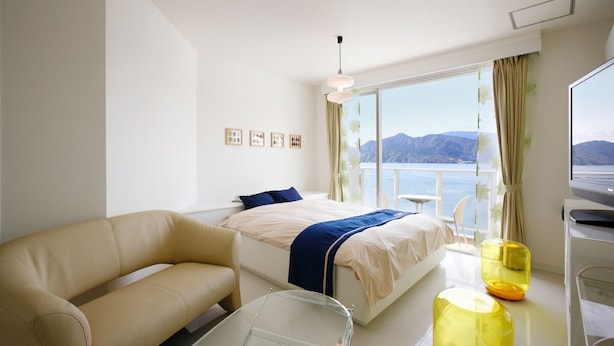 A modern hotel room with a bed, a sofa, a glass table, and a view of the sea. - hotelmare (Kure)