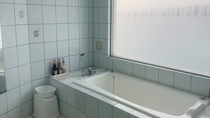 A bathroom with a bathtub, a toilet, and a window. - hotelmare (Kure)