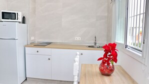 A kitchen with a white refrigerator, a microwave, a wooden countertop, a sink, and a window with a view of buildings. - Nardo studio in the center of Conil (Conil de la Frontera)