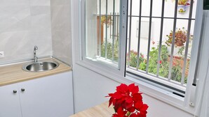 A kitchen with a stainless steel sink, white cabinets, and a window with metal bars. - Nardo studio in the center of Conil (Conil de la Frontera)