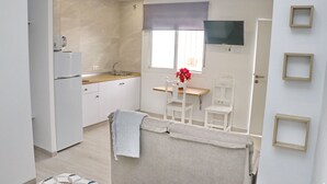 A compact kitchen with a refrigerator, sink, and window. There is a small dining area with a table and chairs. - Nardo studio in the center of Conil (Conil de la Frontera)