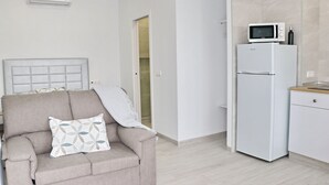A modern living room with a beige sofa, a patterned pillow, a white refrigerator, and a microwave on top. - Nardo studio in the center of Conil (Conil de la Frontera)