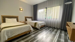 Une chambre d’hôtel avec deux lits, un bureau et une grande fenêtre avec des rideaux.