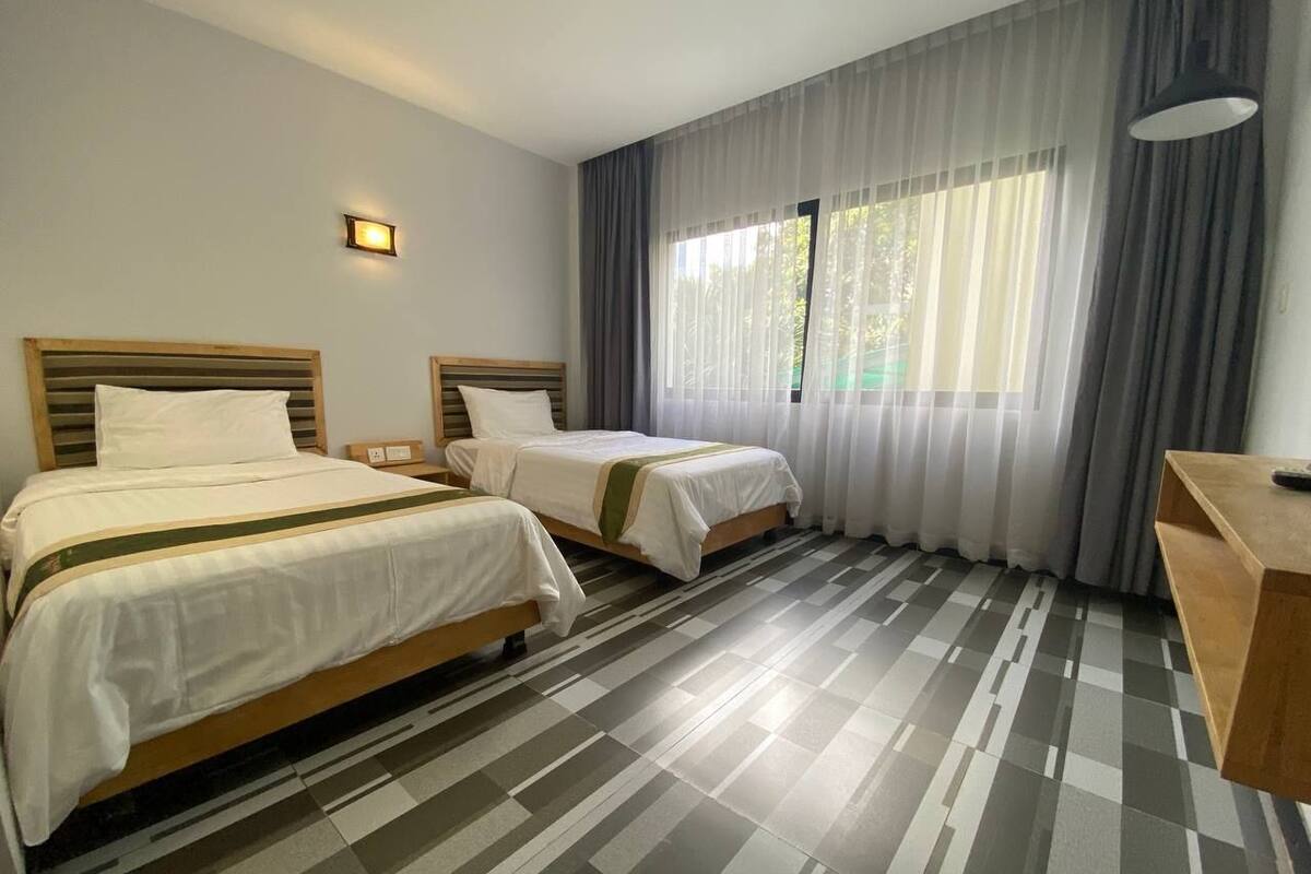 Une chambre d’hôtel avec deux lits, un bureau et une grande fenêtre avec des rideaux.
