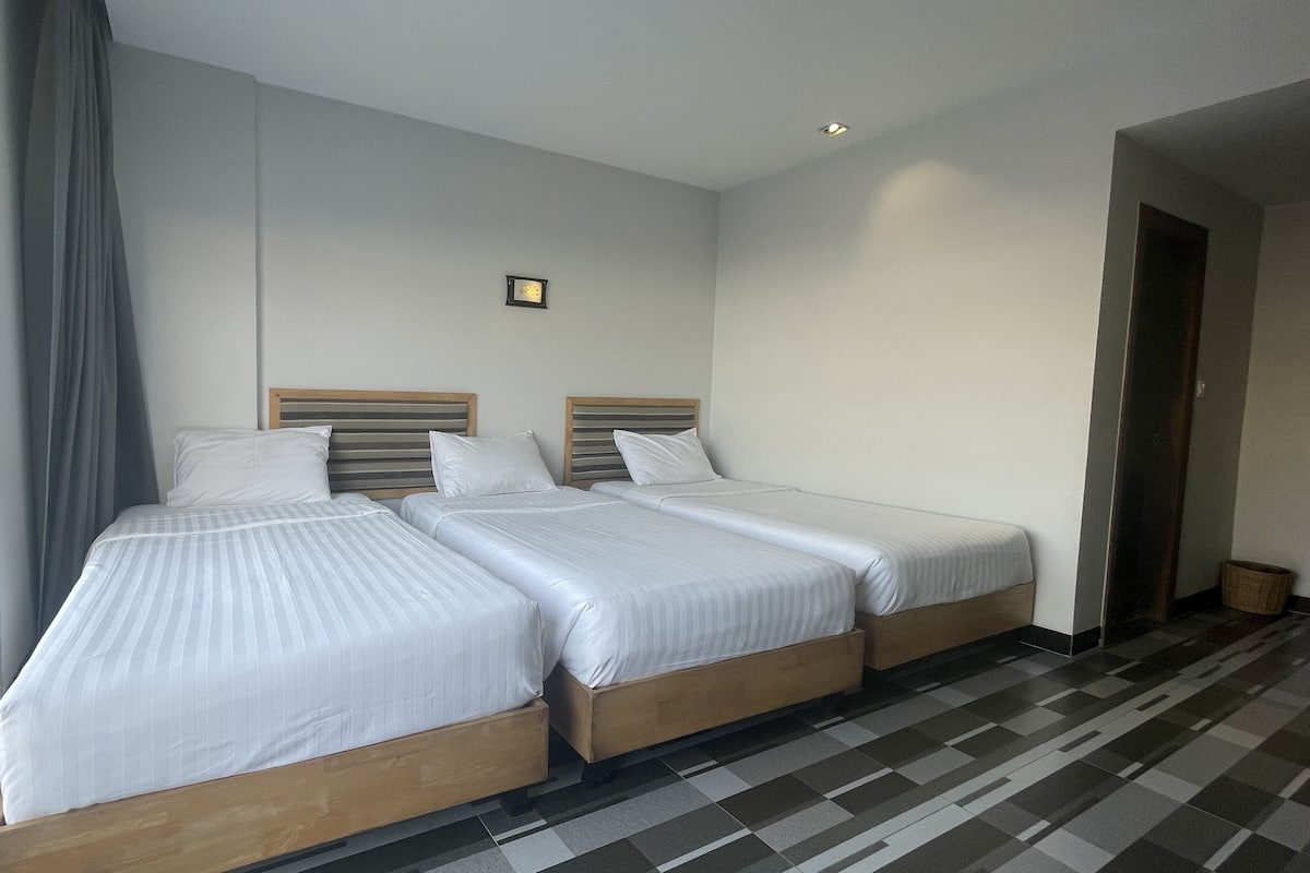 Une chambre d’hôtel avec deux lits simples, une grande fenêtre avec des rideaux, un petit tableau accroché au mur et un sol à carreaux.