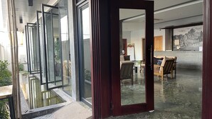 Un hall d’hôtel moderne avec une entrée en verre, un espace repas doté de meubles en bois et une fresque murale.