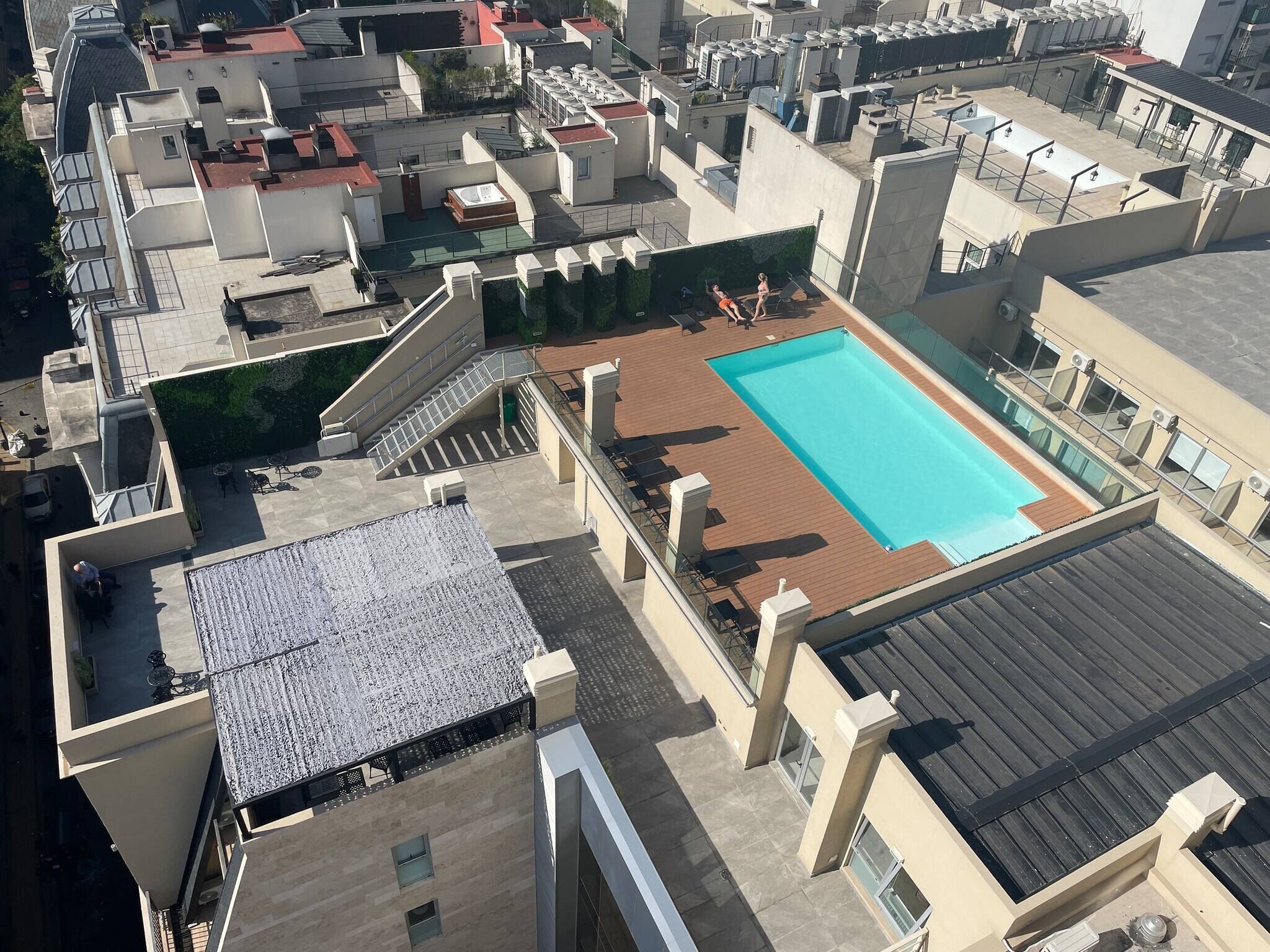 An aerial view of a rooftop with a swimming pool, surrounded by buildings with terraces and balconies.