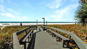 Ein Holzsteg führt zu einem Strand unter blauem Himmel.