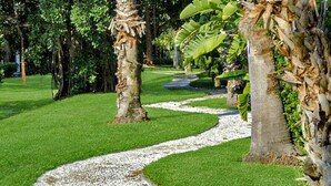 Ein gepflegter Garten mit einem gewundenen Kiesweg, Palmen und saftigem Grün.