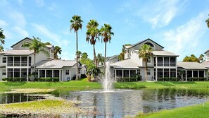 A hotel with a large lawn, a fountain, and tall palm trees.