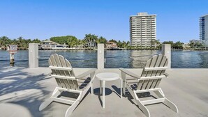 A waterfront patio with two Adirondack chairs and a small table, overlooking a body of water with buildings in the background. - Vistamar Waterfront Beach Abode -walk to the Beach (Fort Lauderdale)