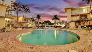 A swimming pool surrounded by lounge chairs and palm trees, with a sunset in the background. - Vistamar Waterfront Beach Abode -walk to the Beach (Fort Lauderdale)