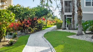 A residential street with a curved driveway, lush greenery, and palm trees. - Relaxing Siesta Key condo - pickleball - 2 heated pools - beach access - GBB 1344 (Siesta Key)