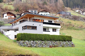 A modern two-story house with a stone retaining wall, a wooden deck, and a view of surrounding houses.