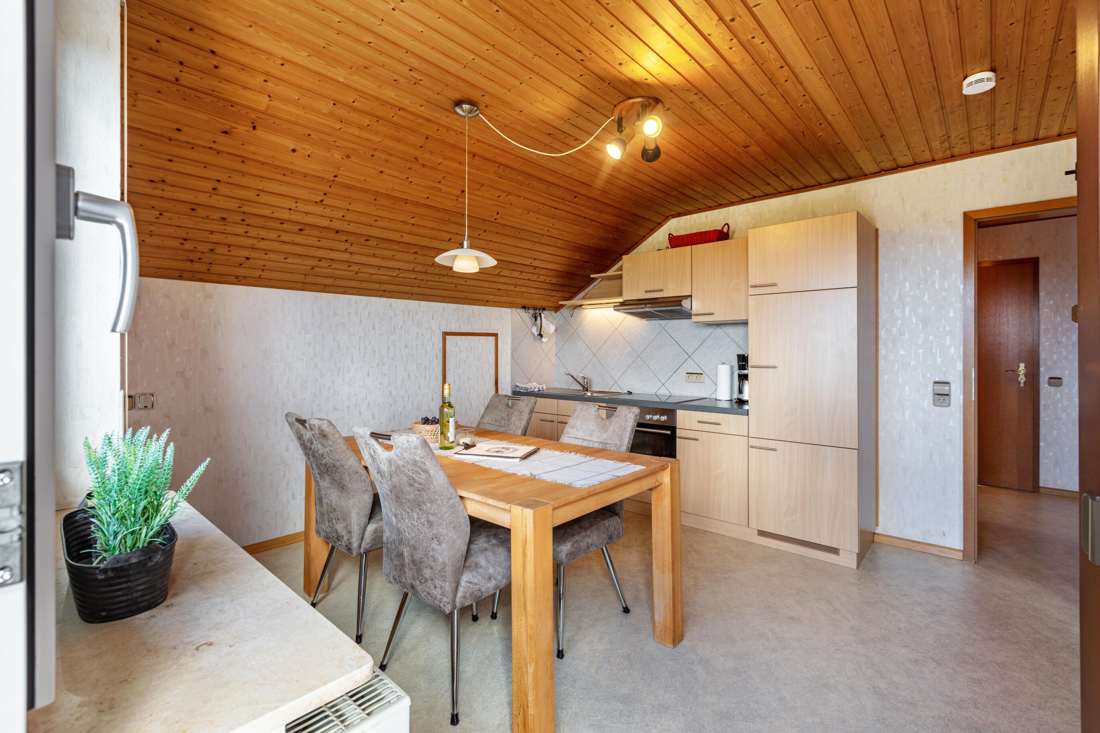 Una cocina moderna con armarios de madera, una mesa de comedor con sillas y un techo con vigas a la vista.