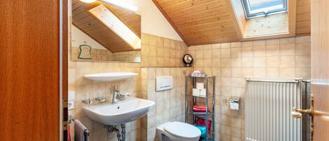 A modern bathroom with a skylight, a sink, a toilet, and a radiator.