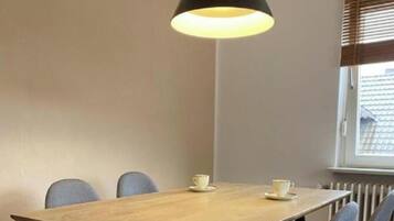 Un comedor con una mesa de madera, cuatro sillas, una lámpara colgante y una ventana con persianas.