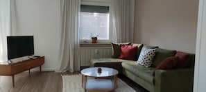 Un salon avec un téléviseur, un canapé, une table basse et une fenêtre avec des rideaux.