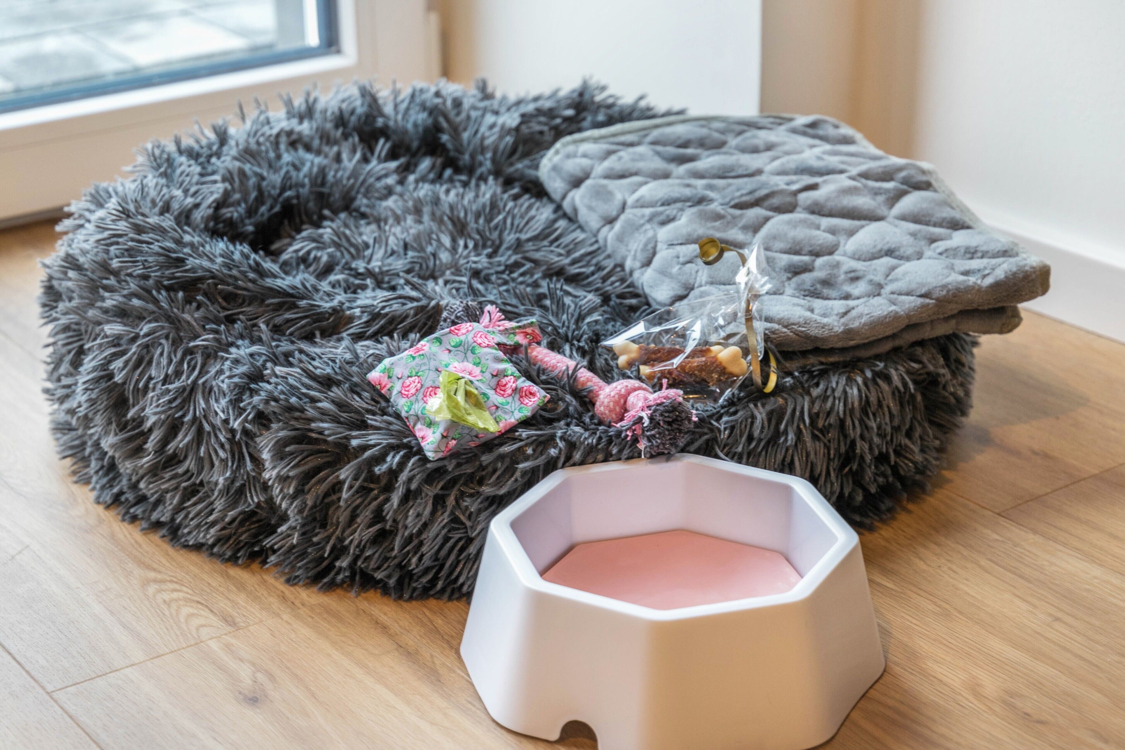 A pet bed with a hexagonal water bowl, a plush toy, and a rolled-up blanket.