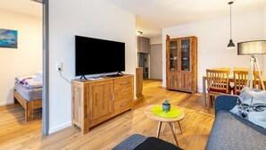 A modern living room with a flat-screen TV, wooden furniture, a dining area, and a staircase leading to another level. - Apartment 'Winderatt 2' with Private Terrace, Shared Garden and Wi-Fi (Husby)