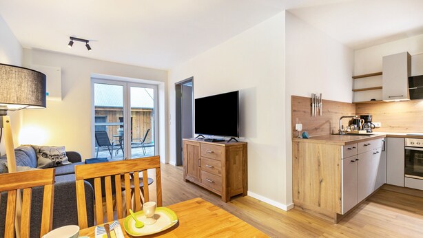 A modern kitchen with wooden cabinets, a dining area with a table and chairs, and a television. - Apartment 'Winderatt 2' with Private Terrace, Shared Garden and Wi-Fi (Husby)