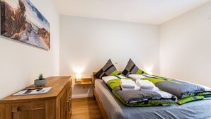 Un dormitorio con cama, mesita de noche, lámpara y un cuadro en la pared.