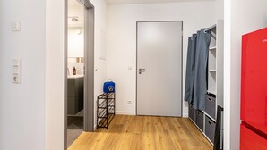 Un pasillo con piso de madera, una puerta blanca, un refrigerador rojo y una bolsa azul sobre un perchero.