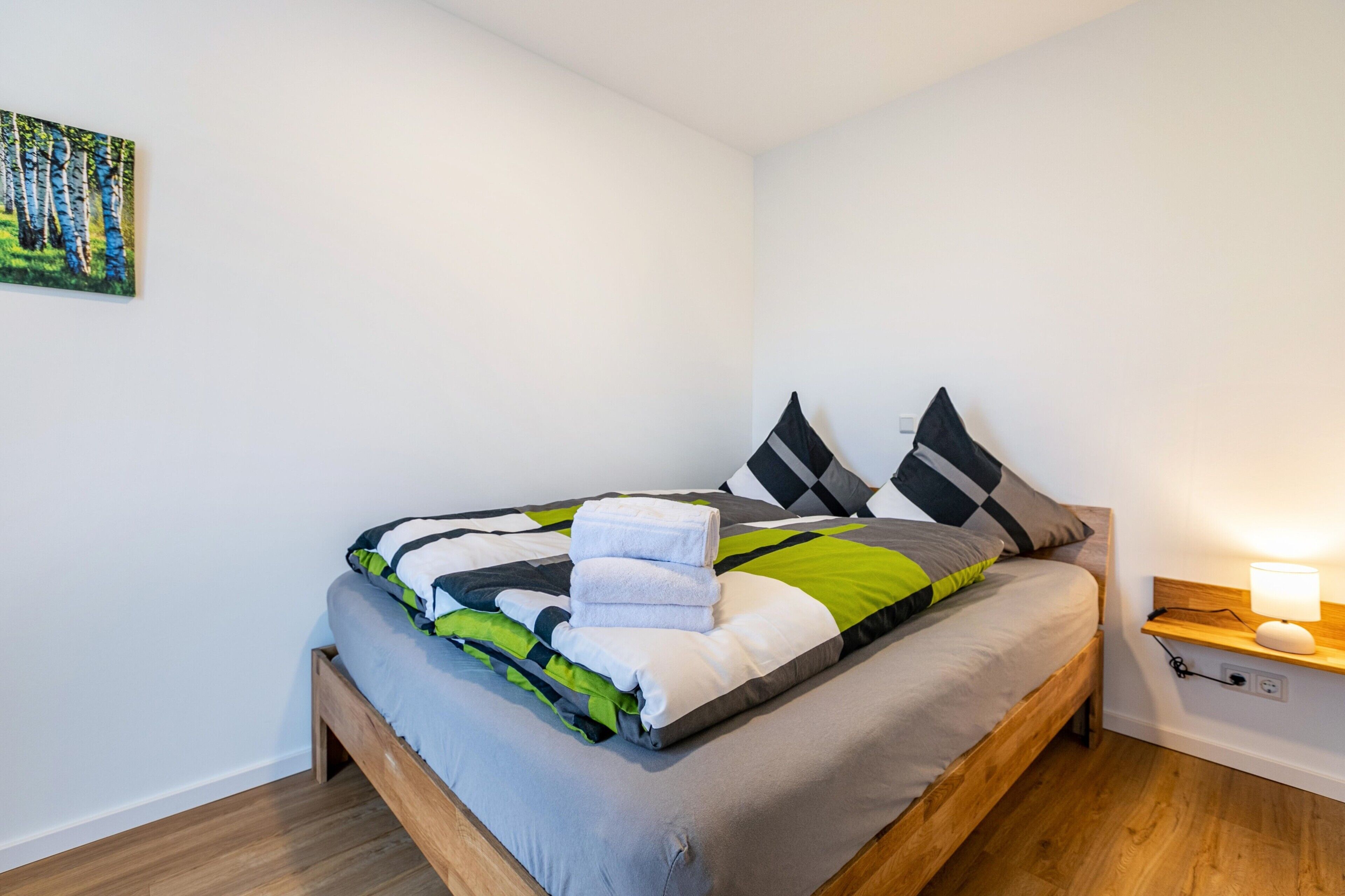 Un letto rifatto con cura, un comodino con una lampada e un quadro appeso al muro.