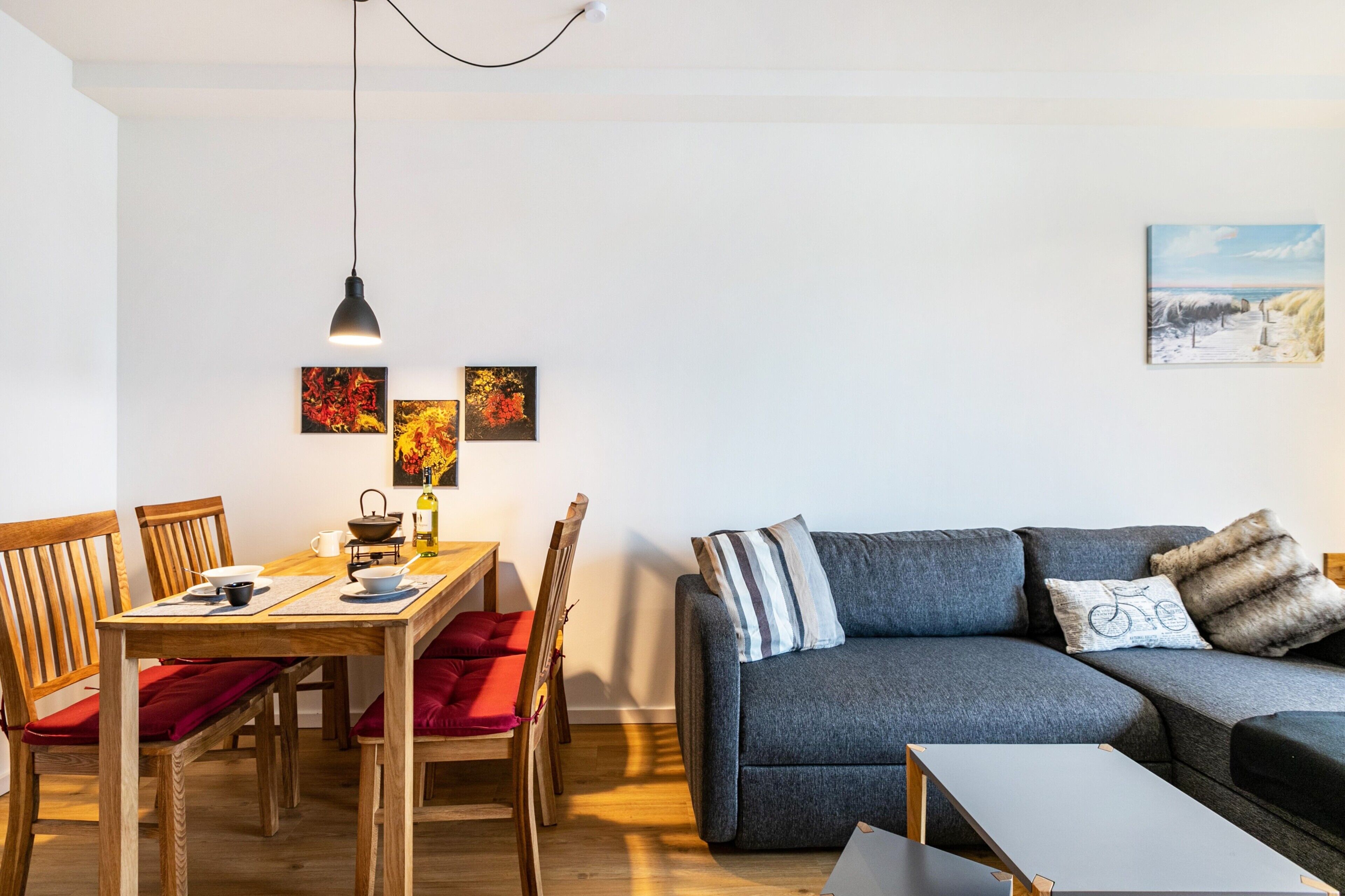 Una sala de estar moderna con sofá, mesa de comedor, sillas y obras de arte en las paredes.