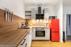 A modern kitchen with a wooden countertop, built-in oven, microwave, and red refrigerator.