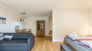 Un salon moderne avec un canapé gris, une table à manger en bois et un lit recouvert de couvertures soigneusement pliées.