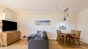 Un salon moderne avec un canapé gris, une table à manger en bois et des chaises. Un téléviseur à écran plat est fixé sur un meuble en bois.