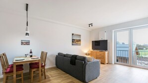 Una sala de estar moderna con sofá, mesa de comedor, sillas, televisor y balcón.